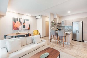 A modern living room with a sofa, a coffee table, and a dining area with a small kitchen in the background. - Santo Domingo Oasis Modern Apartment with Gym u203 (Santo Domingo)