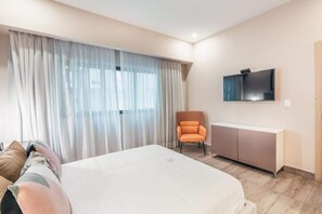 A hotel room with a large bed, a TV mounted on the wall, a chair, and a cabinet. - Santo Domingo Oasis Modern Apartment with Gym u203 (Santo Domingo)