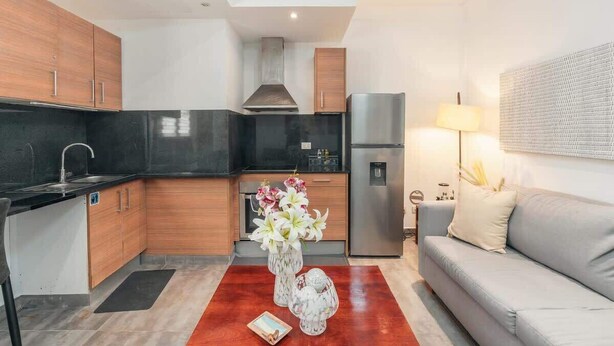 A modern kitchen with wooden cabinets, a black countertop, and a stainless steel refrigerator. There is a dining table with a vase of flowers and a book. - Studio 3 guests Balcony with views Fishing lodge 1090 (Punta Cana)