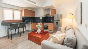 A modern kitchen with dark countertops, wooden cabinets, and stainless steel appliances. There is a dining area with two chairs and a wooden coffee table. A sofa and a lamp are in the living room area. - Studio 3 guests Balcony with views Fishing lodge 1090 (Punta Cana)