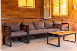 A brick wall, a grey sofa with wooden slats, and a wooden table. - Modern Arvada Hotspot Sauna & Games (Arvada)