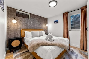 A bedroom with a bed, a round speaker, a wall-mounted air conditioner, and a window with curtains. - Modern Arvada Hotspot Sauna & Games (Arvada)