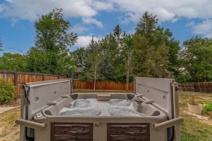 Ein Whirlpool in einem Garten mit Holzzaun, Bäumen und blauem Himmel.