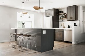 Eine moderne Küche mit einer zentralen Kochinsel, Barhocker und einem integrierten Geschirrspüler.