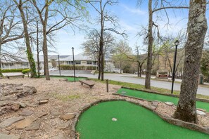A miniature golf course with a green putting area, surrounded by trees and a parking lot. - The Canopy at Table Rock Lake (Kimberling City)