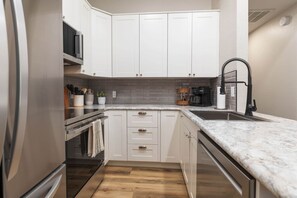 A modern kitchen with white cabinets, a marble countertop, and a built-in oven. - The Canopy at Table Rock Lake (Kimberling City)