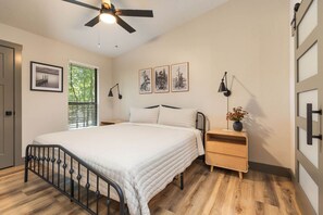 A bedroom with a bed, bedside tables, a ceiling fan, and a window with blinds. - The Canopy at Table Rock Lake (Kimberling City)