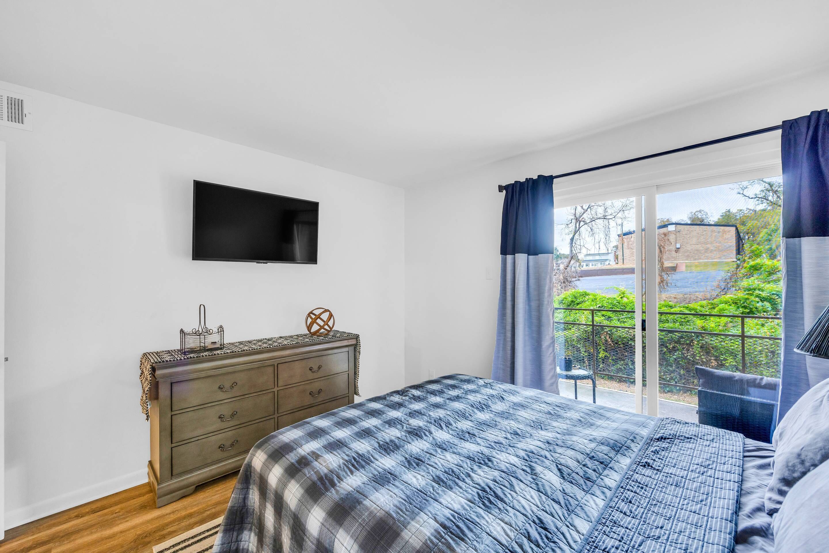 A bedroom with a bed, a dresser, a flat-screen TV, and a view of greenery outside.