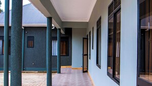 Un corredor cubierto con columnas, piso de baldosas y un edificio con ventanas y puertas.