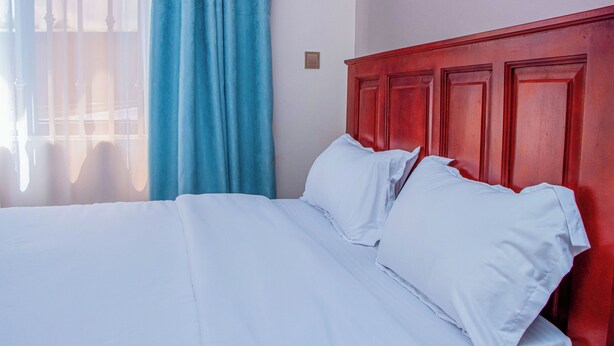 Una cama con ropa blanca, cabecera de madera y una ventana con cortinas azules.