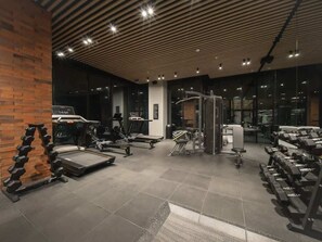 Ein Fitnessraum mit unterschiedlicher Trainingsausstattung, einer Ziegelwand und einer Decke aus Holzlamellen.
