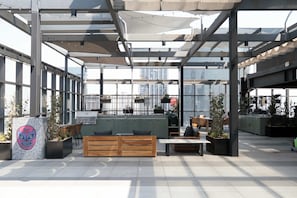 An outdoor seating area with wooden benches and tables, surrounded by planters and a large window offering views of the city. - Cozy Furnished Studio in Mexico City U203 (Ciudad de México)