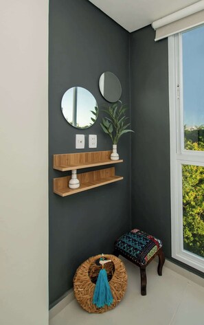 Ein Eckzimmer mit dunkler Wand, zwei runden Spiegeln, Holzregalen, einer Topfpflanze, einem Weidenhocker und einer Bank mit gemustertem Kissen.