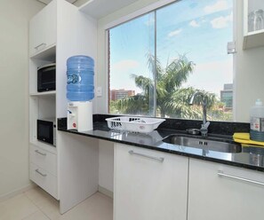 Eine moderne Küche mit weißen Schränken, einer schwarzen Arbeitsplatte, einem Wasserspender, einer Spüle und einem Fenster mit Blick auf Palmen.