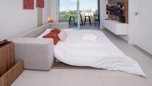 A modern bedroom with a sofa bed, a TV, and a balcony with a view. - Stylish 1BR with Urban Vista (Asunción)