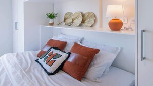 A bedroom with a bed, white cabinets, a shelf with decorative items, and a lamp. - Stylish 1BR with Urban Vista (Asunción)