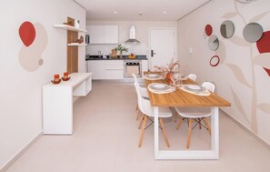 Una cuina moderna amb armaris blancs, una taula de dinar de fusta i una cadira sense respatller blanca.