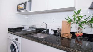 A kitchen with a washing machine, a microwave, a sink, and a plant. - Stylish 1BR with Urban Vista (Asunción)