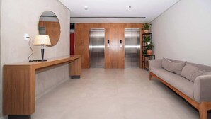 A modern lobby with a reception desk, a round mirror, a sofa, and two elevators. - Stunning 1BR Apt with amazing City Views (Asunción)