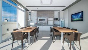 A modern meeting room with a long table, chairs, a kitchen area, and a large window. - Stunning 1BR Apt with amazing City Views (Asunción)