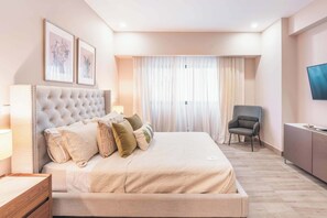 Une chambre avec un grand lit, une chaise, un téléviseur et des œuvres d’art accrochées au mur.
