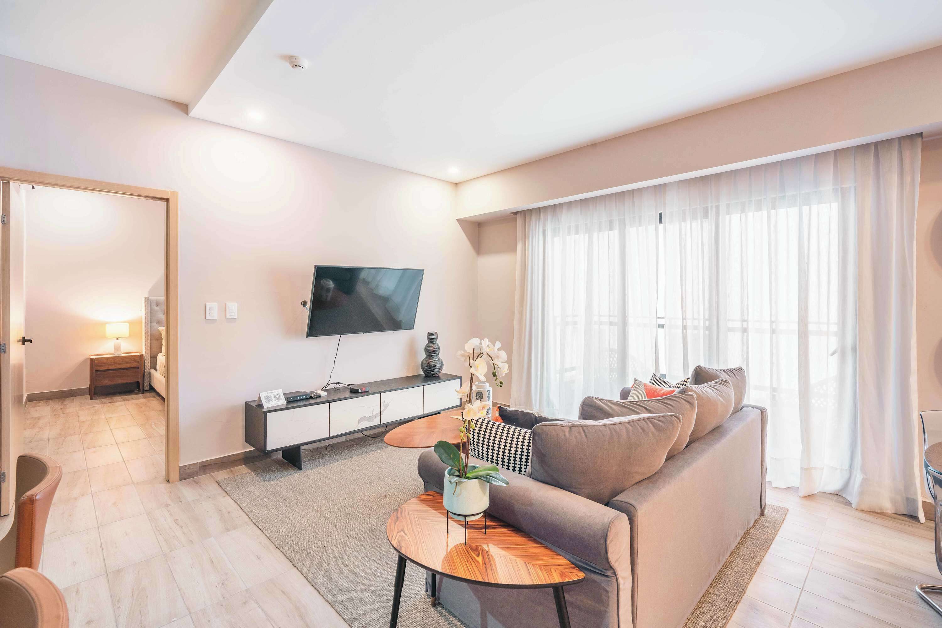 A modern living room with a sofa, coffee table, TV, and a large window with curtains.