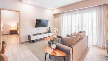 A modern living room with a sofa, coffee table, TV, and a large window with curtains.