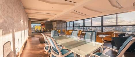 A modern conference room with a glass table and chairs, large windows with a city view, and a high ceiling with exposed beams.