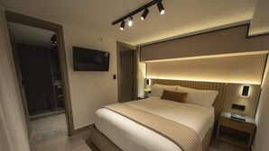 Ein modernes Hotelzimmer mit einem großen Bett, Nachttischen, einem Flachbildfernseher und einem begehbaren Kleiderschrank.