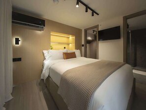 Ein modernes Hotelzimmer mit einem großen Bett, einem Flachbildfernseher und einer eingebauten Klimaanlage.