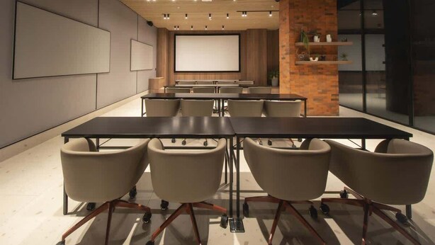 Een vergaderzaal met een lange tafel, zes stoelen, een projectiescherm en een accentmuur van baksteen.