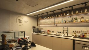 Een moderne bar met een strak aanrecht, een glazen vitrine en diverse flessen op planken.