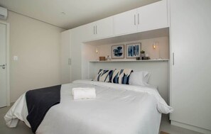 A bedroom with a bed, white wardrobe, and shelves with decorative items. - Modern 1BR with Desk & Panoramic View (Asunción)