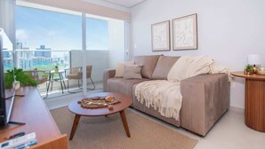 Una sala de estar moderna con un sofá, una mesa de centro y vistas de la ciudad a través de grandes ventanales.