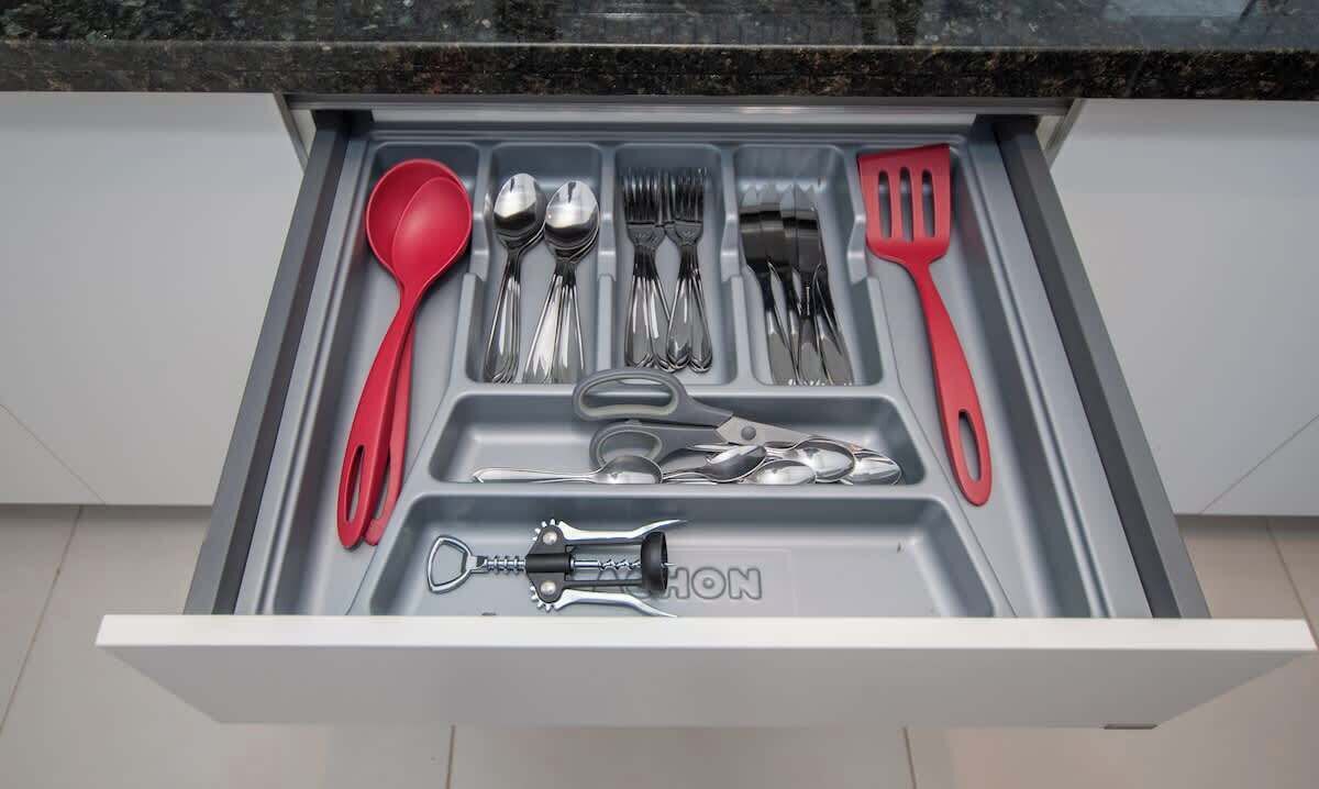 Un cajón con cubiertos y un sacacorchos.