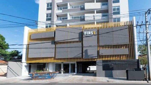 Un edificio de varios pisos con un diseño arquitectónico moderno, que presenta una entrada destacada con fachada amarilla y negra.