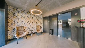 Eine moderne Lobby mit Wandmustern, zwei Ledersessel, ein Mülleimer und eine runde Leuchte.