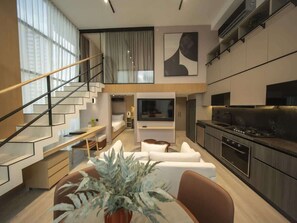 Et moderne interiør med trappe, opholdsstue med sofa og spisebord, samt et køkken med komfur og skabe.