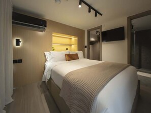 Et moderne hotelværelse med seng, sengeborde, et vægmonteret TV og en aircondition.