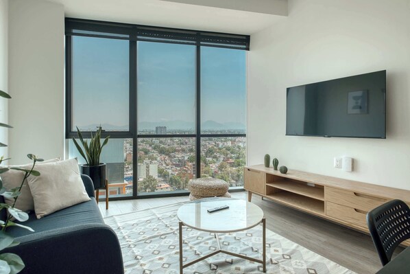 Een moderne woonkamer met een groot raam, een bank, een salontafel, een televisie en een houten tv-meubel.