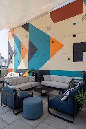A modern outdoor seating area with a geometric mural, a sofa, chairs, and a small table. - Furnished Studio in Mexico City (Ciudad de México)