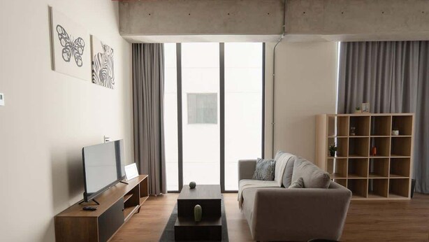 Ein modernes Wohnzimmer mit einer Couch, einem Couchtisch, einem Fernseher auf einem Schrank und einem Bücherregal.