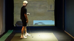 Ein Raum mit einer Projektionsleinwand, einem Golfwagen und Sportgeräten.