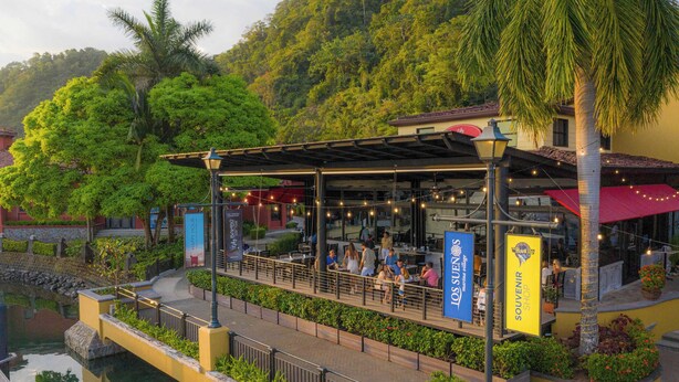 Ein Restaurant mit Außenbereich, das auf ein Gewässer mit üppiger Vegetation und einer Hügelkulisse blickt.