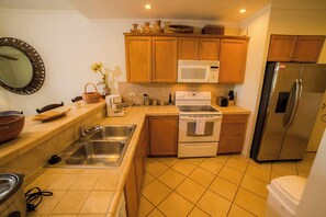 Una cocina con gabinetes de madera, microondas, estufa, fregadero y refrigerador.