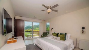 Une chambre moderne avec un grand lit, un bureau, une chaise, une télévision et un balcon donnant sur un espace verdoyant.