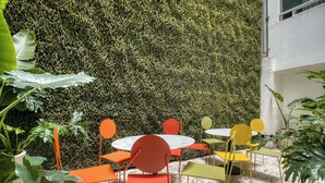 A patio area with round tables and chairs, surrounded by a lush green wall. - Modern King Studio in Central Roma Norte (Ciudad de México)
