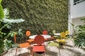 A patio area with round tables and chairs, surrounded by a lush green wall. - Modern King Studio in Central Roma Norte (Ciudad de México)
