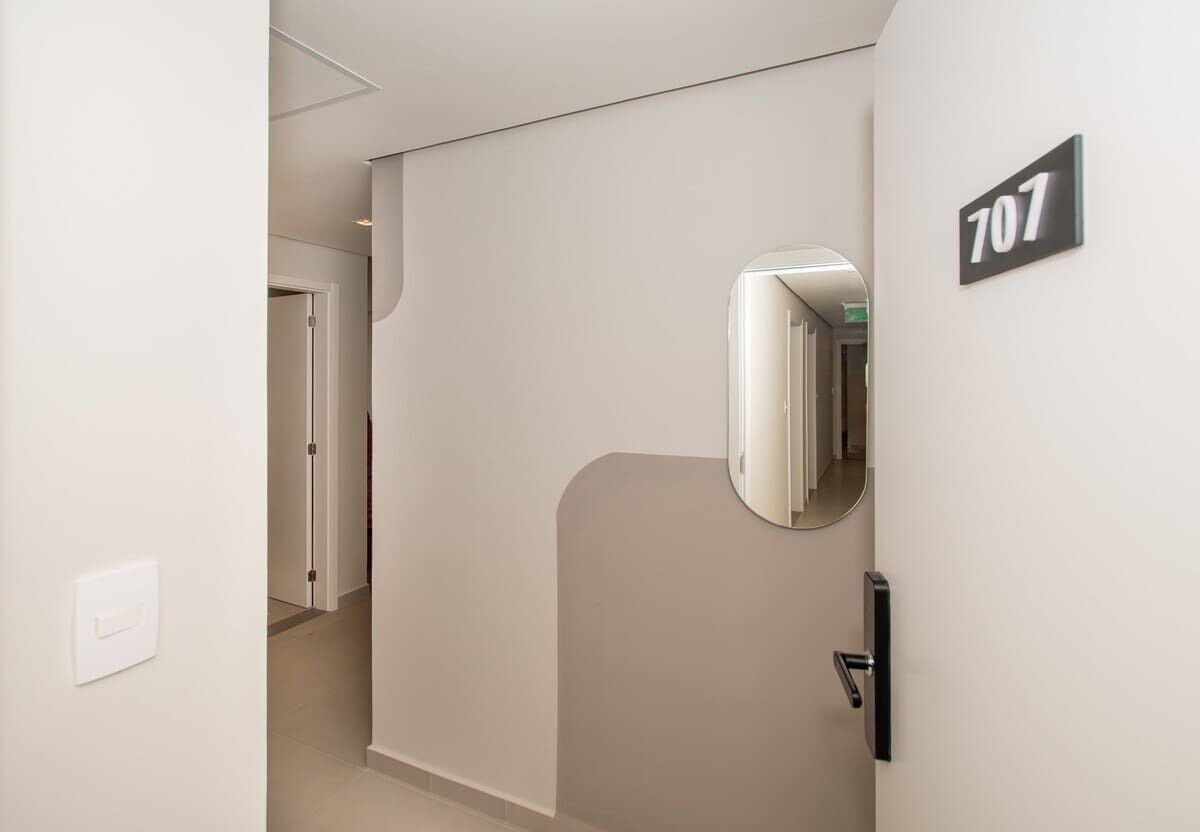Een gang met een deur waarop '707' staat, een lichtschakelaar en een spiegel.