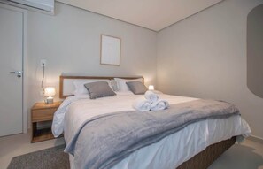 Ein ordentlich bezogenes Bett mit grauer Decke, zwei Nachttischlampen und einem gerahmten Bild an der Wand.
